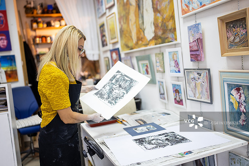 自信而自豪的白人女艺术家在观察她制作的石版画图片素材