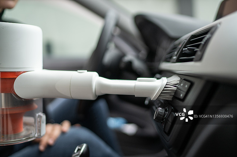 女人用手持吸尘器清洁汽车仪表盘的特写图片素材