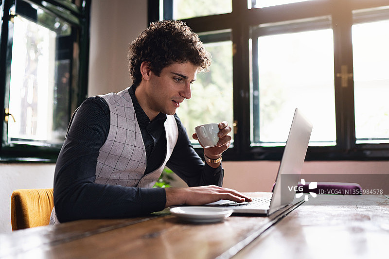 年轻商人在现代餐厅喝咖啡并使用笔记本电脑工作图片素材