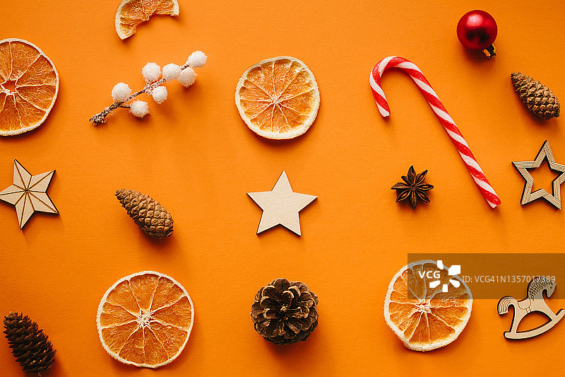 由木头、糖果手杖、肉桂棒、干橙和松果制成的天然圣诞冬季装饰品，橙色背景。图片素材