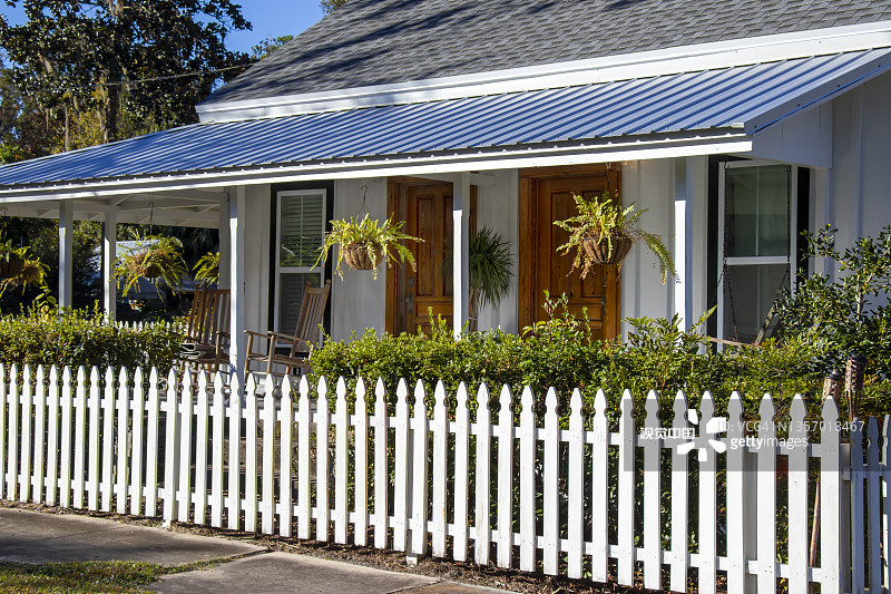 悬挂的蕨类植物、木制摇椅、两扇橡木门和白色尖桩篱笆，营造出佛罗里达州怀特斯普林斯历史悠久的翻新木结构房屋的迷人入口图片素材