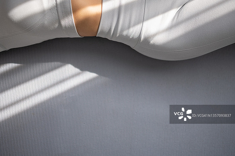 一位美丽女人的纤细腰肢穿着运动服躺在灰色地毯上，留有文案空间图片素材