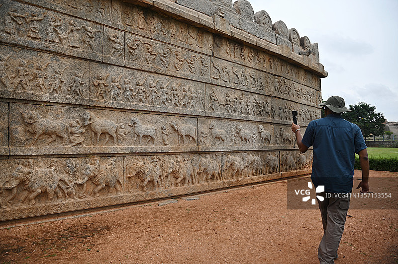 男人用他的运动相机拍摄古石庙墙壁上各种动物的石雕图片素材