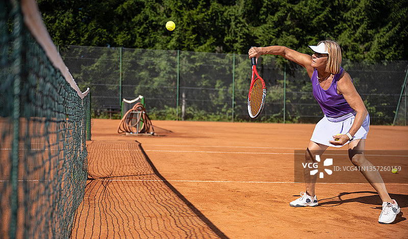 运动中的女人，在红土球场上打网球的健康老年妇女图片素材