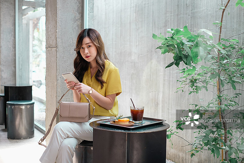 在咖啡馆椅子上放松、用智能手机发短信的微笑亚洲年轻女性，享受咖啡馆的放松时刻图片素材