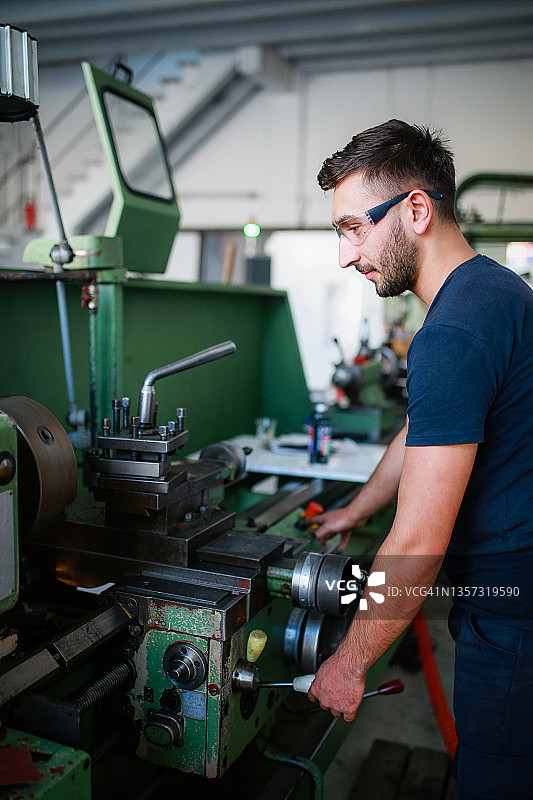 戴安全帽和反光服的年轻男机械工人在工厂车床旁工作图片素材