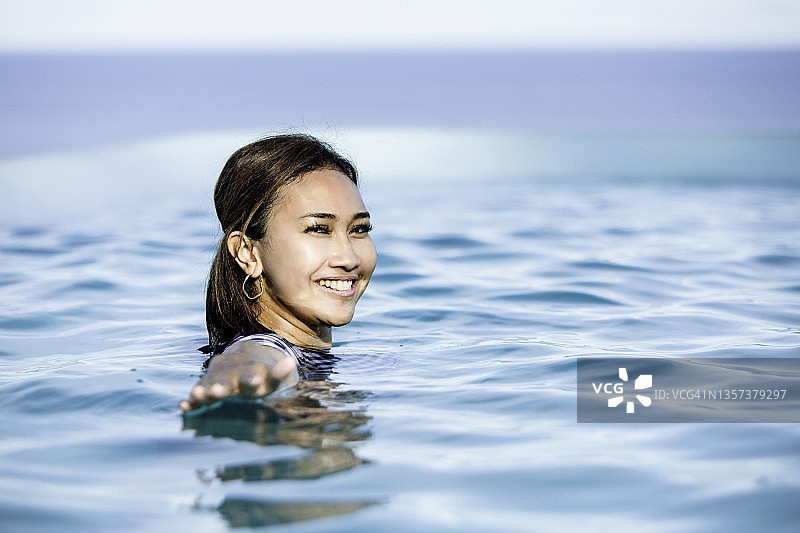 年轻亚洲女子在泳池中游泳，眺望海上的船只图片素材