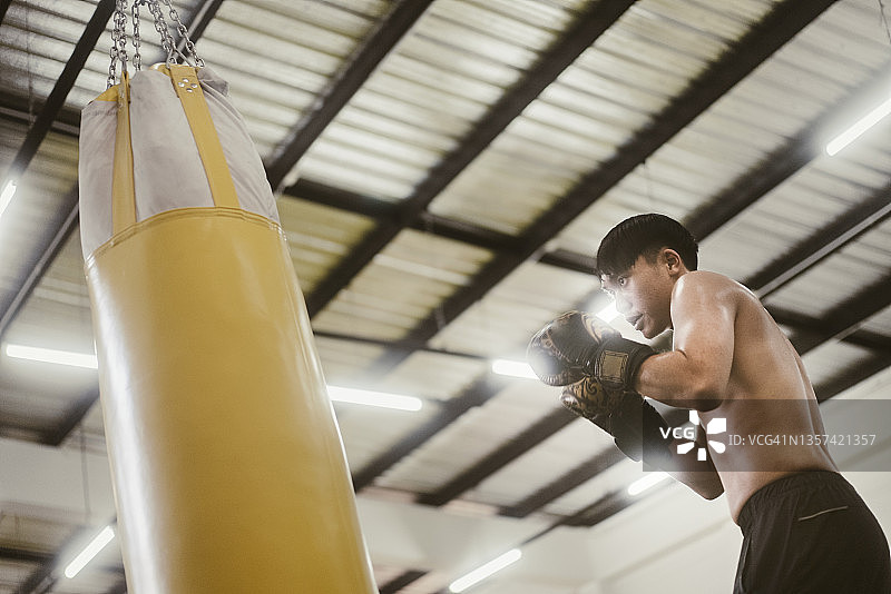 在拳击馆练习拳击并用黄色沙袋击打的亚洲青年拳击手图片素材