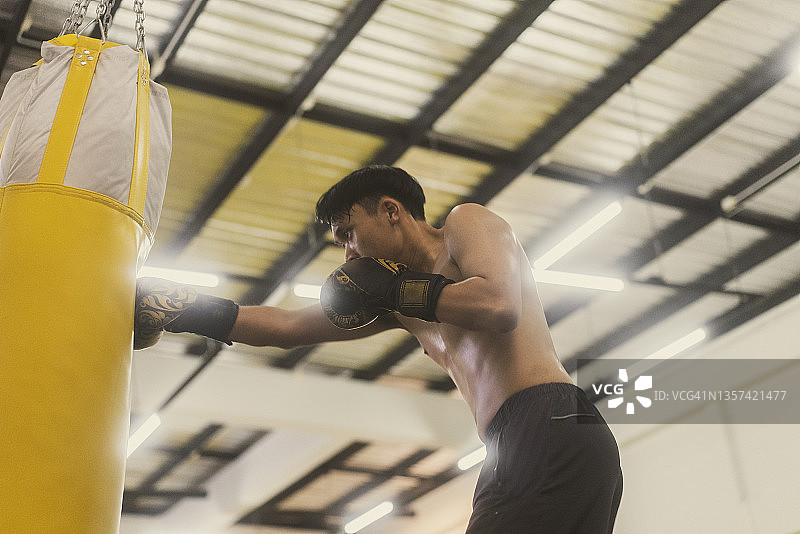 在拳击馆练习拳击并用黄色沙袋击打的亚洲青年拳击手图片素材