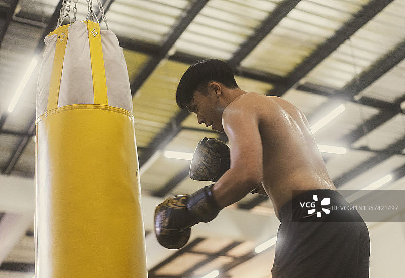 在拳击馆练习拳击并用黄色沙袋击打的亚洲青年拳击手图片素材