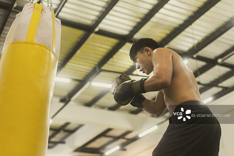 在拳击馆练习拳击并用黄色沙袋击打的亚洲青年拳击手图片素材