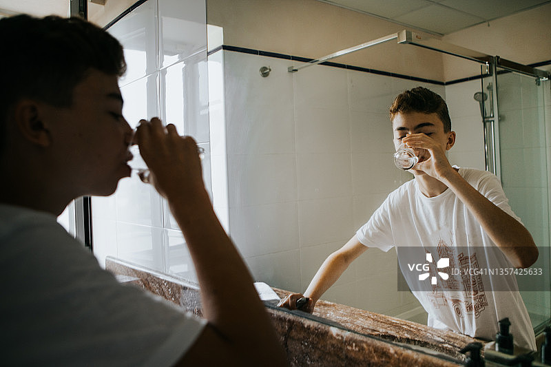 年轻的西班牙裔青少年在浴室喝自来水图片素材