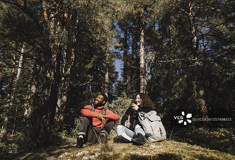 在阳光明媚的森林里和男朋友一起拿着饮料坐着的快乐女人图片素材