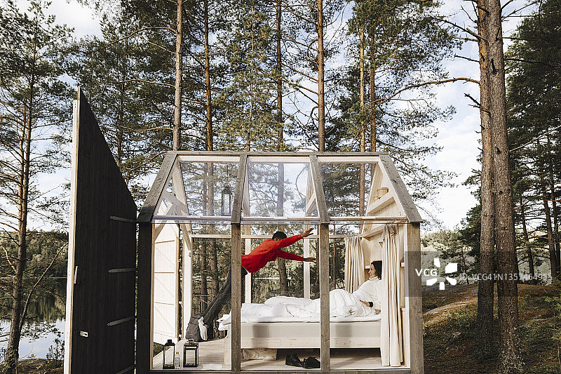 男人跳跃，女友躺在玻璃小屋的床上图片素材