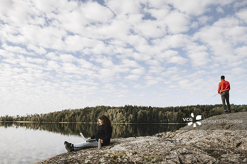 女人在湖边远程办公，男友在钓鱼图片素材