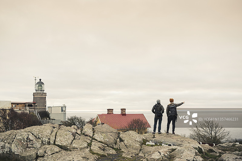 日落时，与男性朋友站在岩石上指向大海的男子背影图片素材