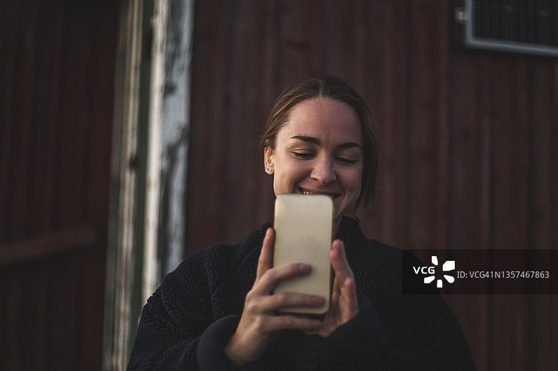 对着小屋用智能手机自拍的微笑女人图片素材