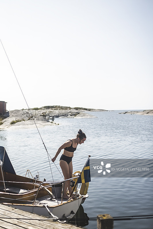 阳光明媚的日子里，中年妇女身穿比基尼站在帆船上图片素材