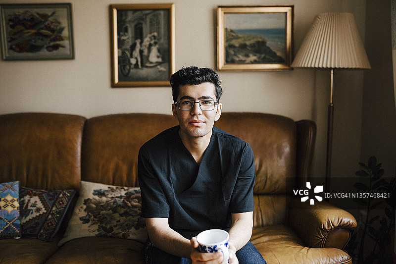 在客厅里手持咖啡杯的年轻男护士肖像图片素材