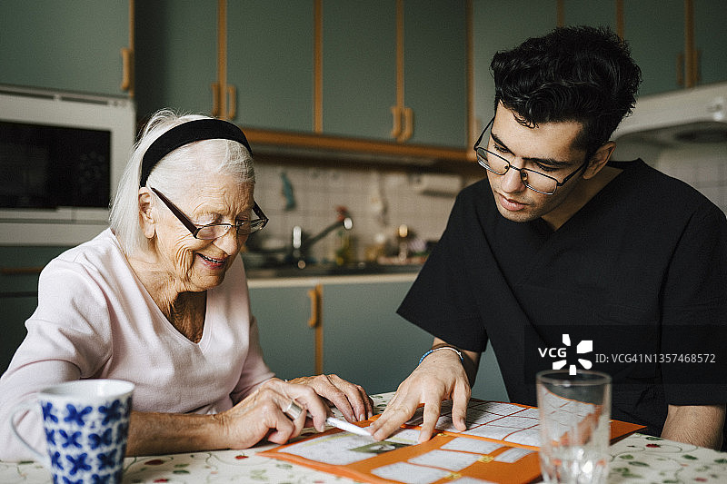 年轻男医护人员在厨房里和老年妇女一起玩填字游戏图片素材