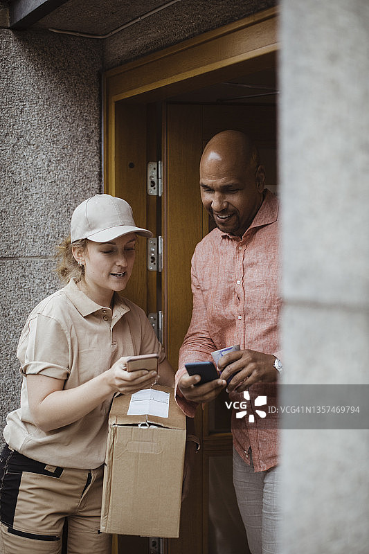 年轻的送货女工和男顾客在门口使用智能手机图片素材