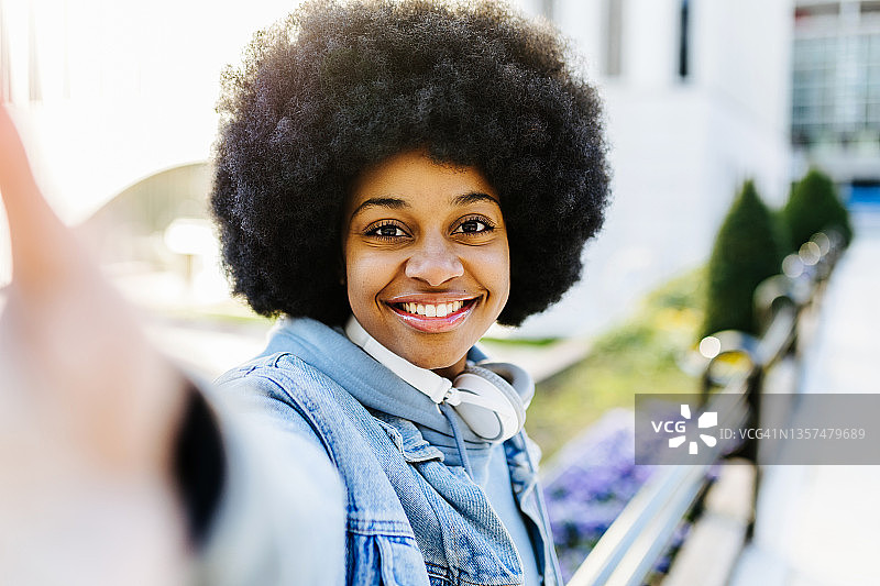 微笑的漂亮年轻女人在户外用智能手机自拍图片素材