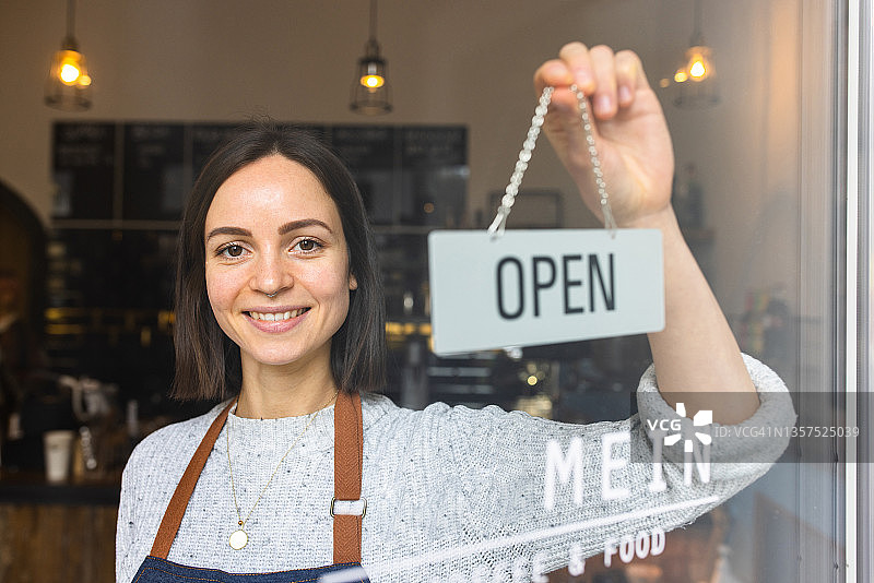 快乐的女店主在咖啡馆挂着“营业中”的牌子图片素材