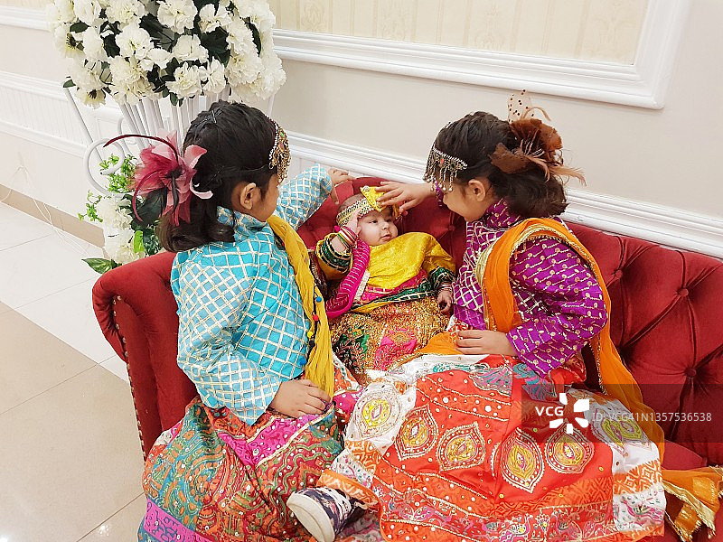 两个穿着彩色派对礼服的小女孩在照顾她们的妹妹图片素材