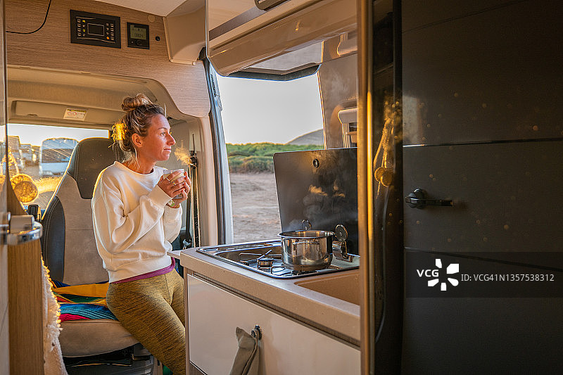 女人在面包车里喝茶，欣赏日出时的海景图片素材