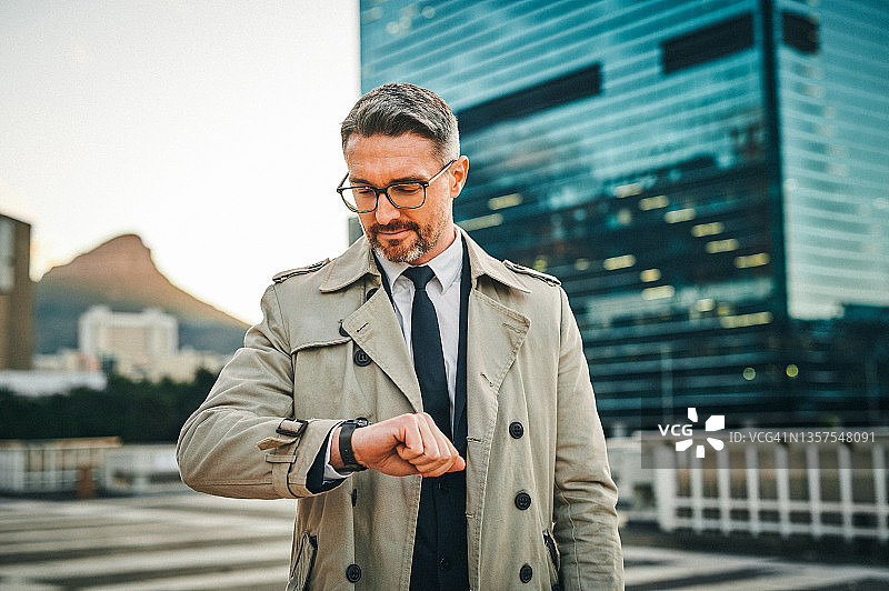 中年商人站在城市里查看手表时间照片图片素材