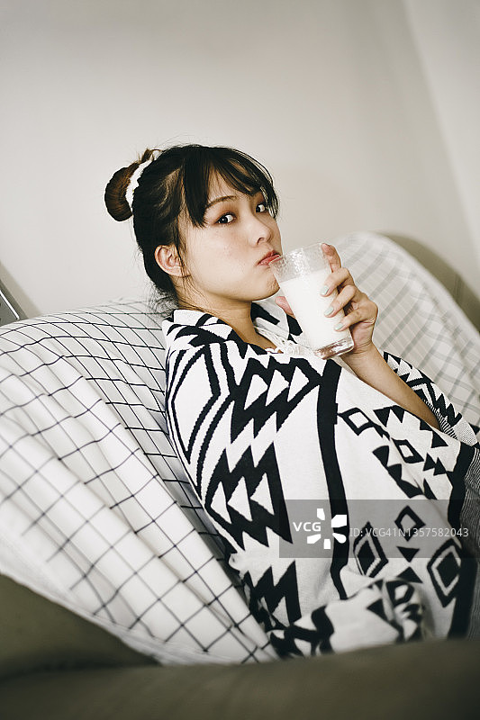 清晨，美丽的亚洲女孩在沙发上喝牛奶图片素材