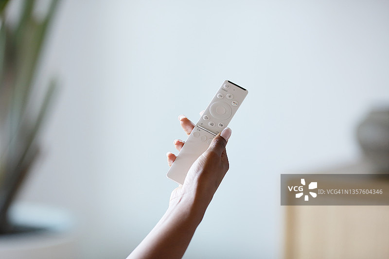 非裔美国年轻女子手持白色遥控器对准智能电视的特写图片素材