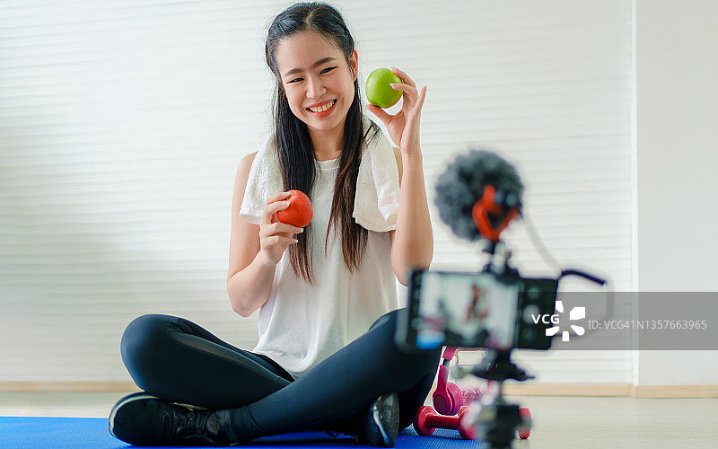 美丽的亚洲健康博主展示苹果和健康饮食，在家录制视频直播图片素材