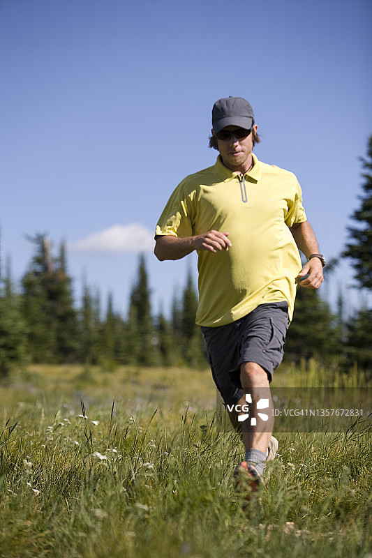 男子在落基山脉高处徒步时穿过草地图片素材