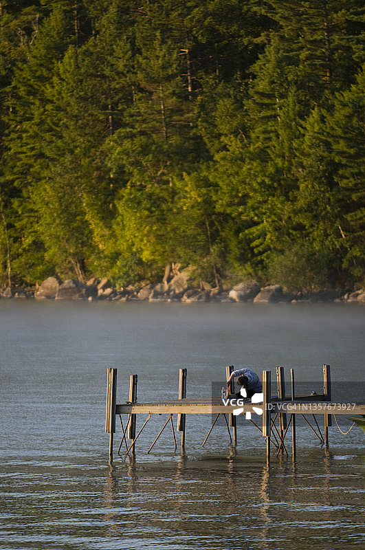黎明时分，一名妇女在缅因州塞巴戈湖的码头上伸展身体图片素材