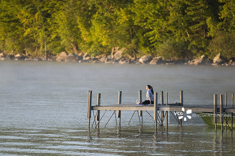 黎明时分，一名妇女在缅因州塞巴戈湖的码头上伸展身体图片素材