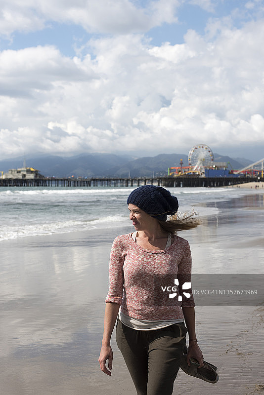 在阴天沿着海滩行走的微笑女子图片素材