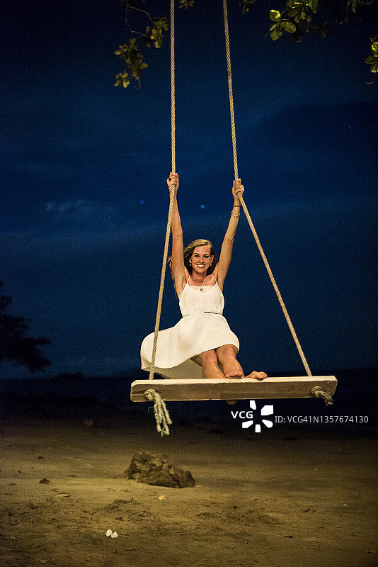 夜晚，女人站在海滩的树秋千上图片素材
