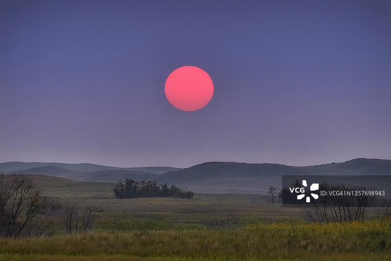内布拉斯加州情人节镇以南沙丘上，日落时分被附近野火染成红色的大球图片素材