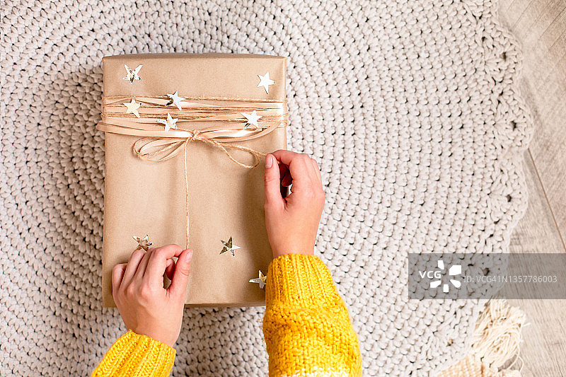 身穿白黄色毛衣的女人在针织地毯上打开纸质礼品盒，新年庆祝概念，俯视特写图片素材