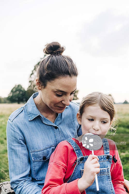 母亲看着女儿在公园里吃棒棒糖图片素材