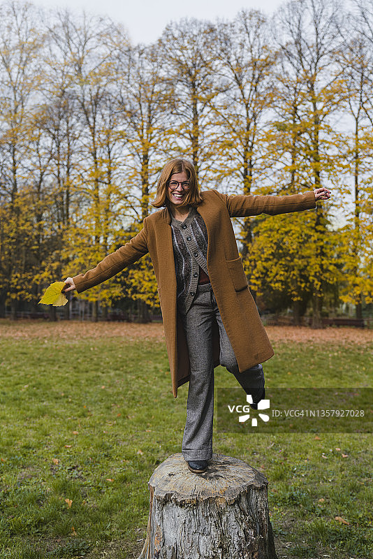 在公园里在树桩上保持平衡的嬉戏的年轻女子图片素材