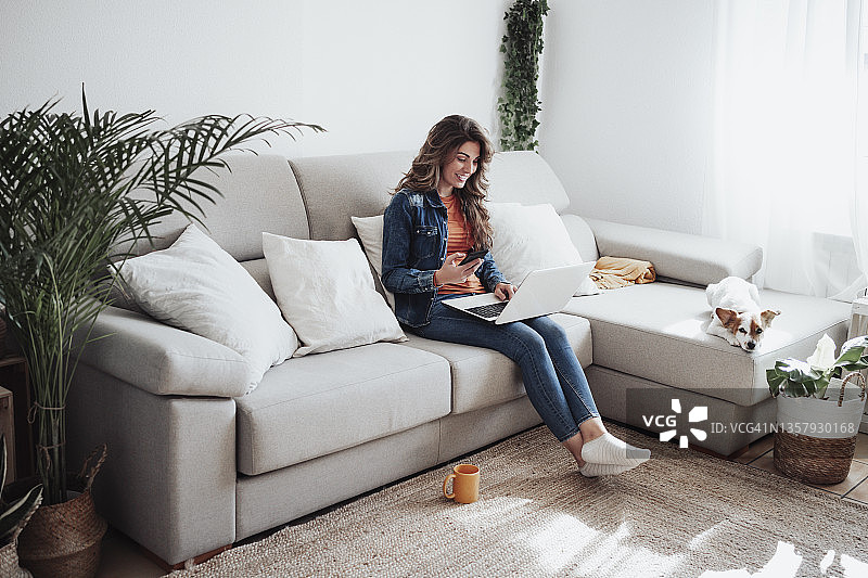 在沙发上用笔记本电脑的微笑女人图片素材