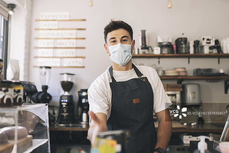 戴防护口罩的收银员在咖啡馆手持信用卡读卡器图片素材