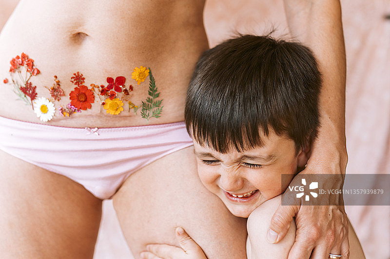 儿子拥抱母亲，母亲剖腹产疤痕处有花朵纹身图片素材