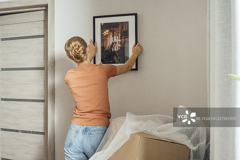 女子在新公寓的墙上安装相框图片素材