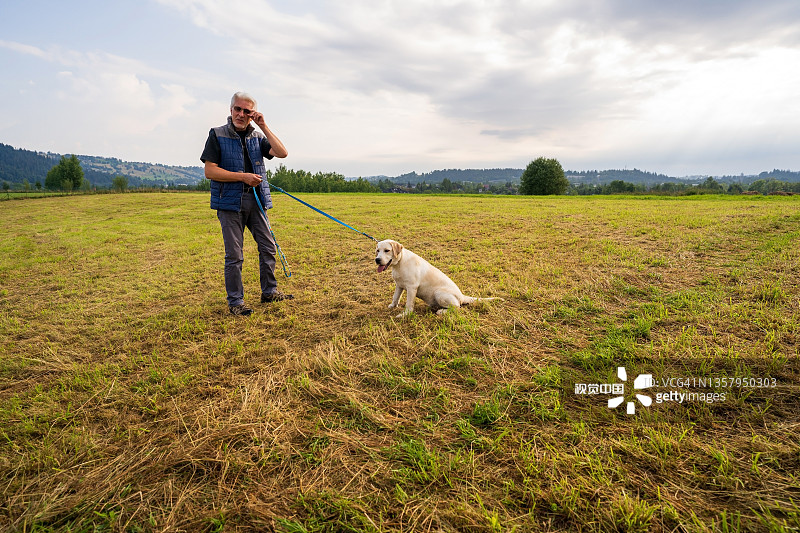 男人牵着拉布拉多犬站在绿色田野里图片素材