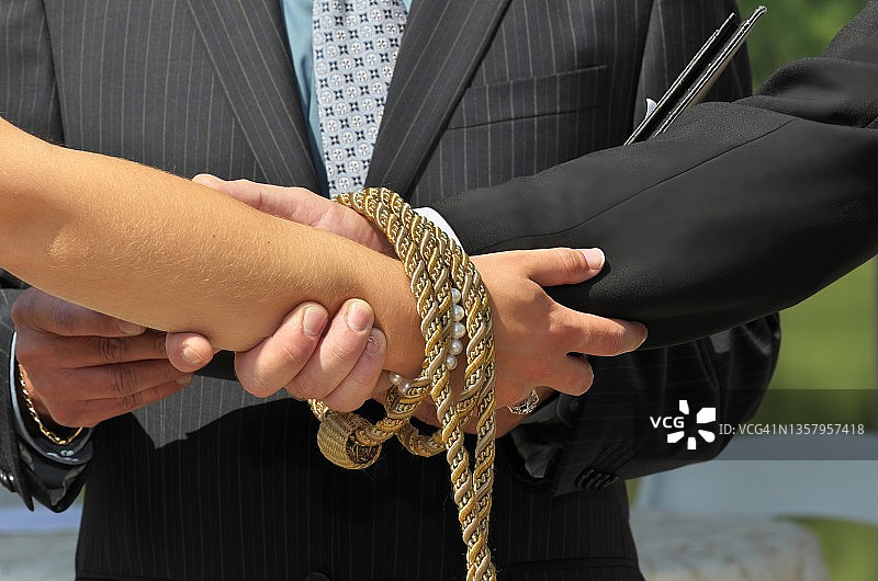 手fasting仪式上，被编织绳索缠绕的新娘和新郎牵手图片素材