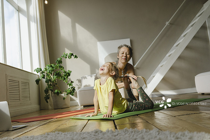 母亲在家中帮助女孩在运动垫上锻炼图片素材