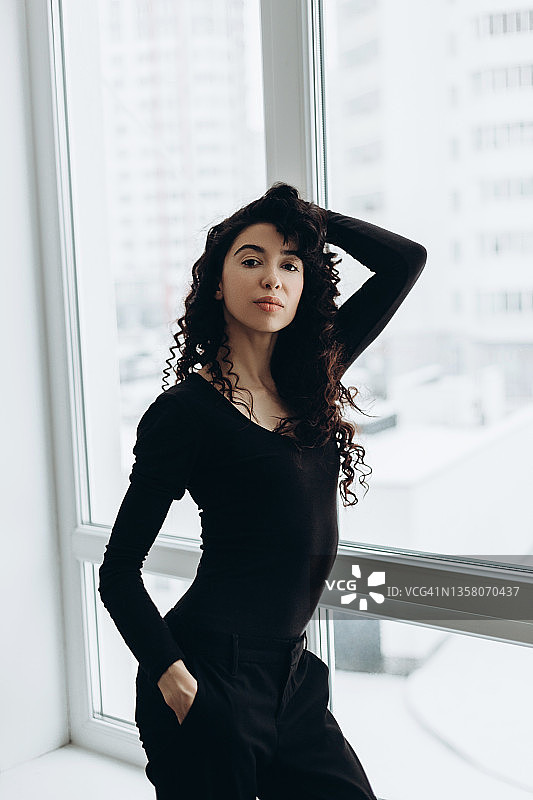倚靠窗户的深色卷发年轻女人图片素材